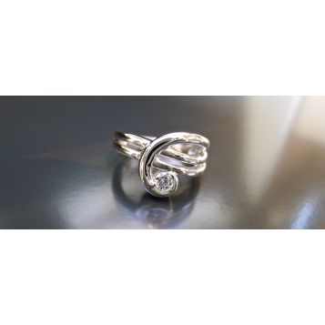 Precious metal formed into a ribbon and forged into a ring that swirls up to hold a perfect diamond